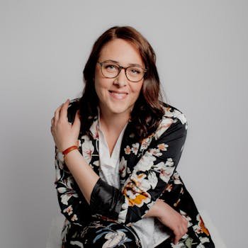 Professional portrait of a smiling woman in a stylish floral suit with glasses.