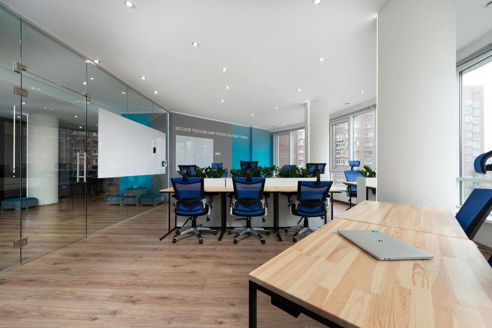 Spacious and contemporary office featuring glass walls, blue chairs, and wooden desks.